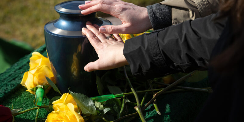 Hands,Touching,A,Burial,Urn,In,A,Bright,Outdoor,Funeral